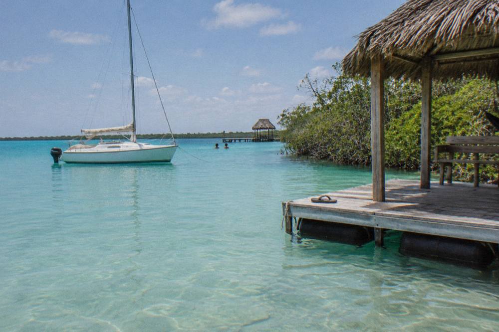 Sailboat and pontoon anchored in shallow turquoise water near a mangrove line on Bacalar lagoon