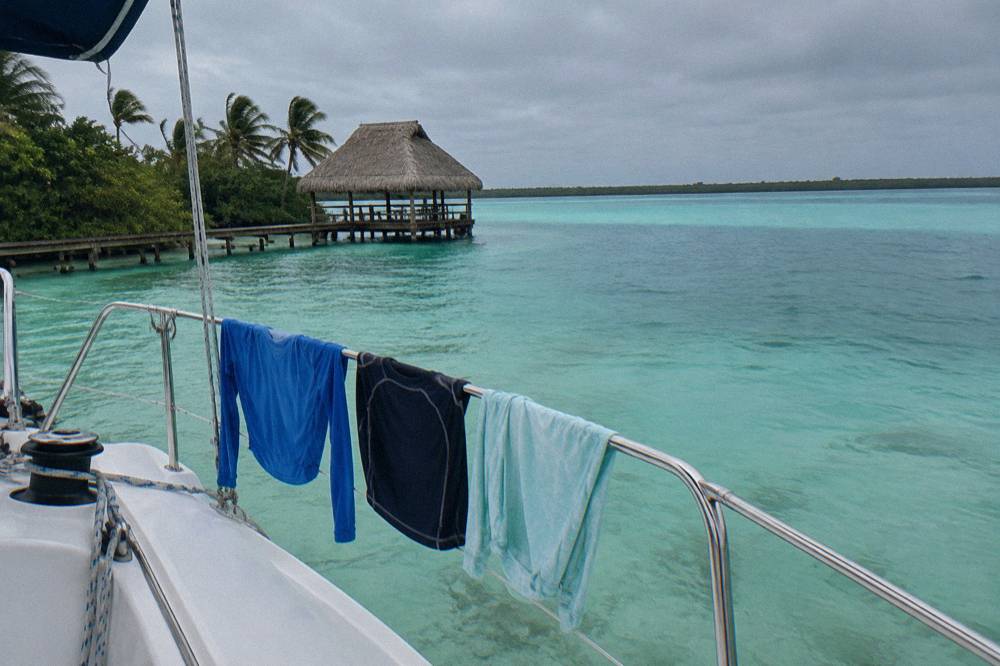 Long sleeve UV swim shirts drying on a rail beside a moored sailboat on Bacalar Lagoon