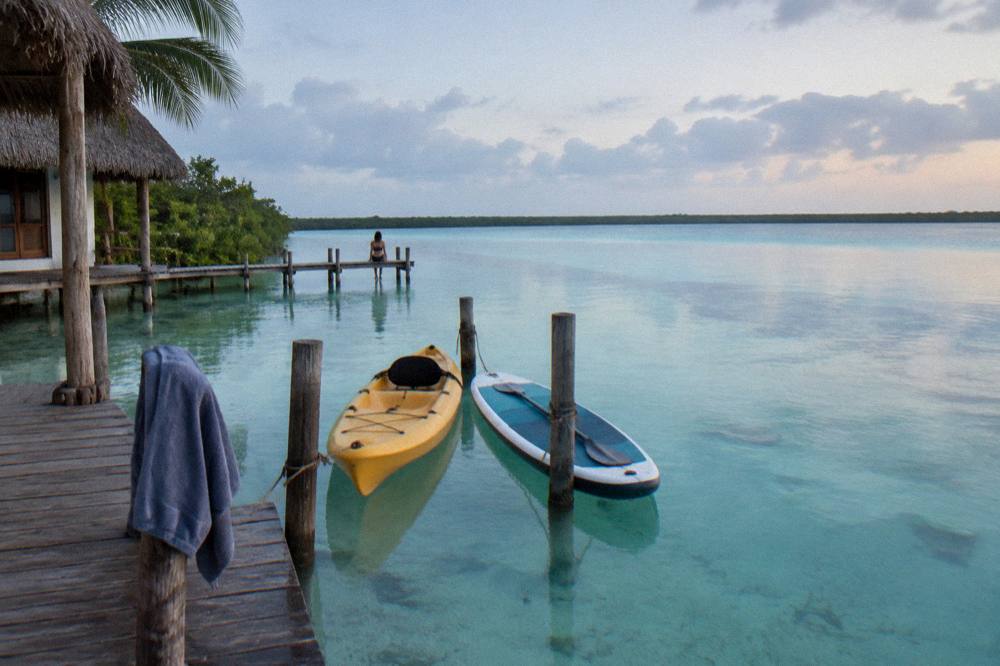 A kayak and paddleboard tied at a small pier at dawn with calm turquoise water beyond