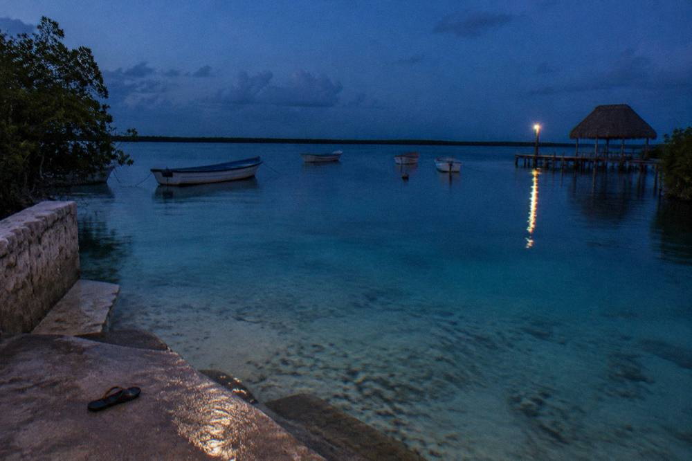 Row of small boats at anchor on glassy lagoon water at dusk