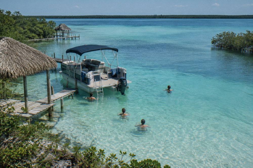 Small pontoon boat anchored in shallow turquoise water while passengers swim