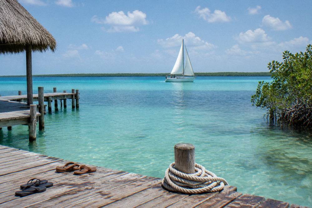 Sailboat with white sails raised gliding across calm blue-green lagoon water