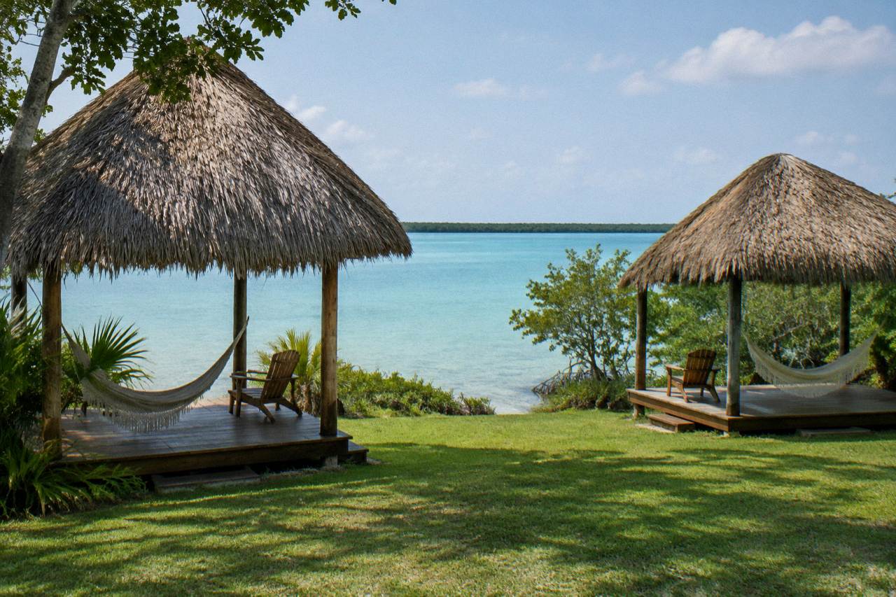 Thatched palapa cabanas with wooden decks on a lawn beside the Bacalar Lagoon shore