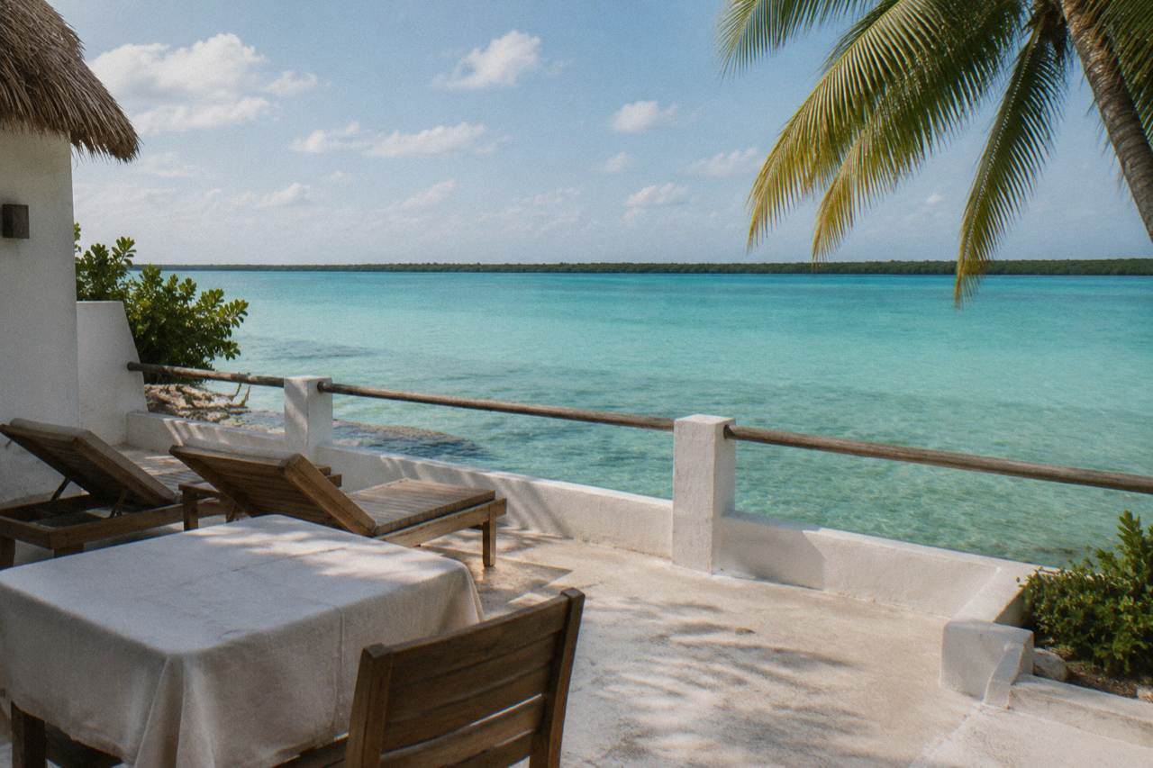 A whitewashed lagoon-front hotel terrace with loungers overlooking turquoise Bacalar Lagoon