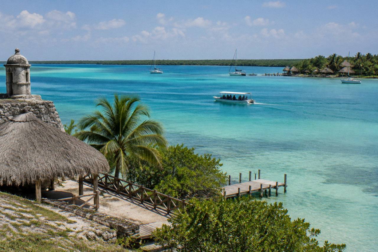 A small tour boat gliding over the turquoise bands of Bacalar Lagoon